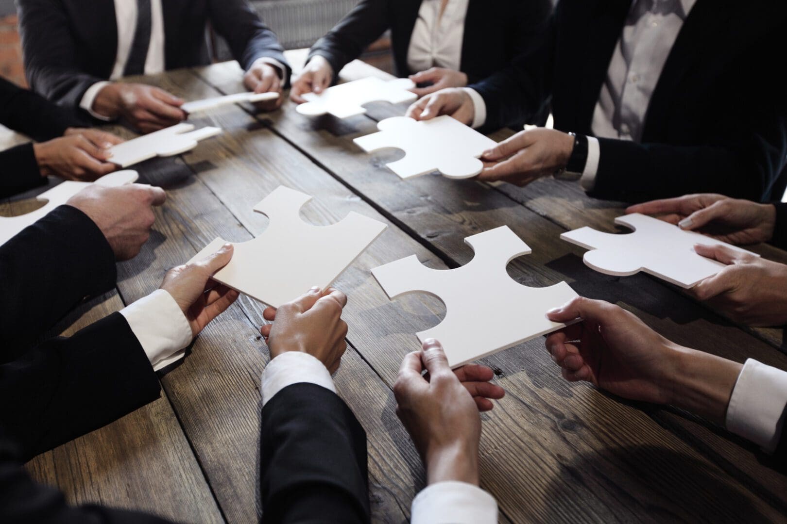 Business people and puzzle on wooden table, teamwork concept